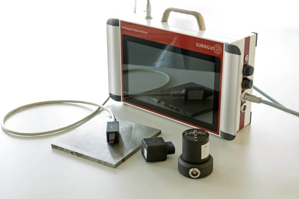 Photo of Barkhausen Noise Analyzer from SURAGUS with a metal plate and 3 different sensor heads available for optimal results.